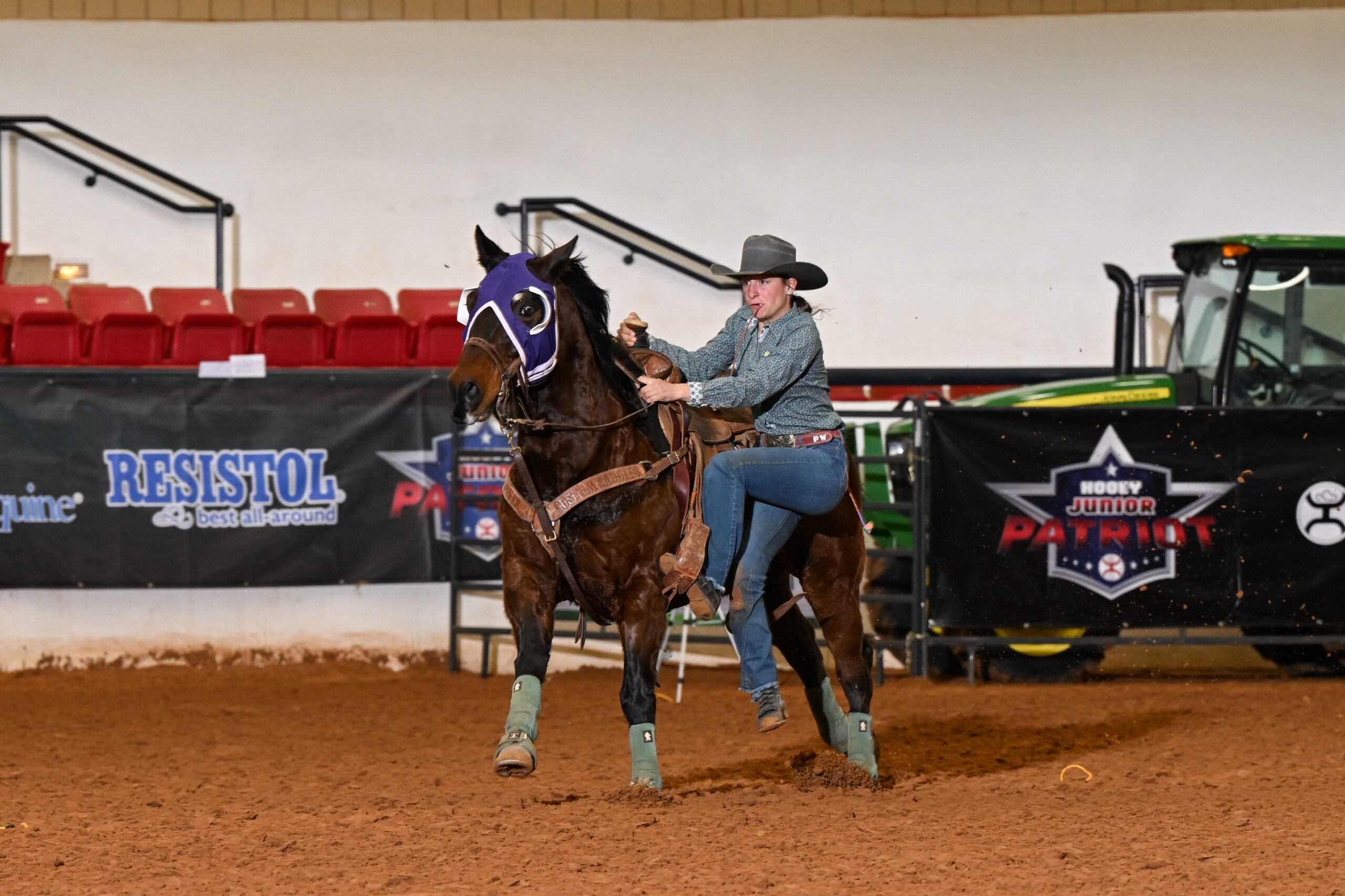 Cowboy on horseback wearing purple horse mask and gray cowboy hat rides across dirt arena during rodeo event