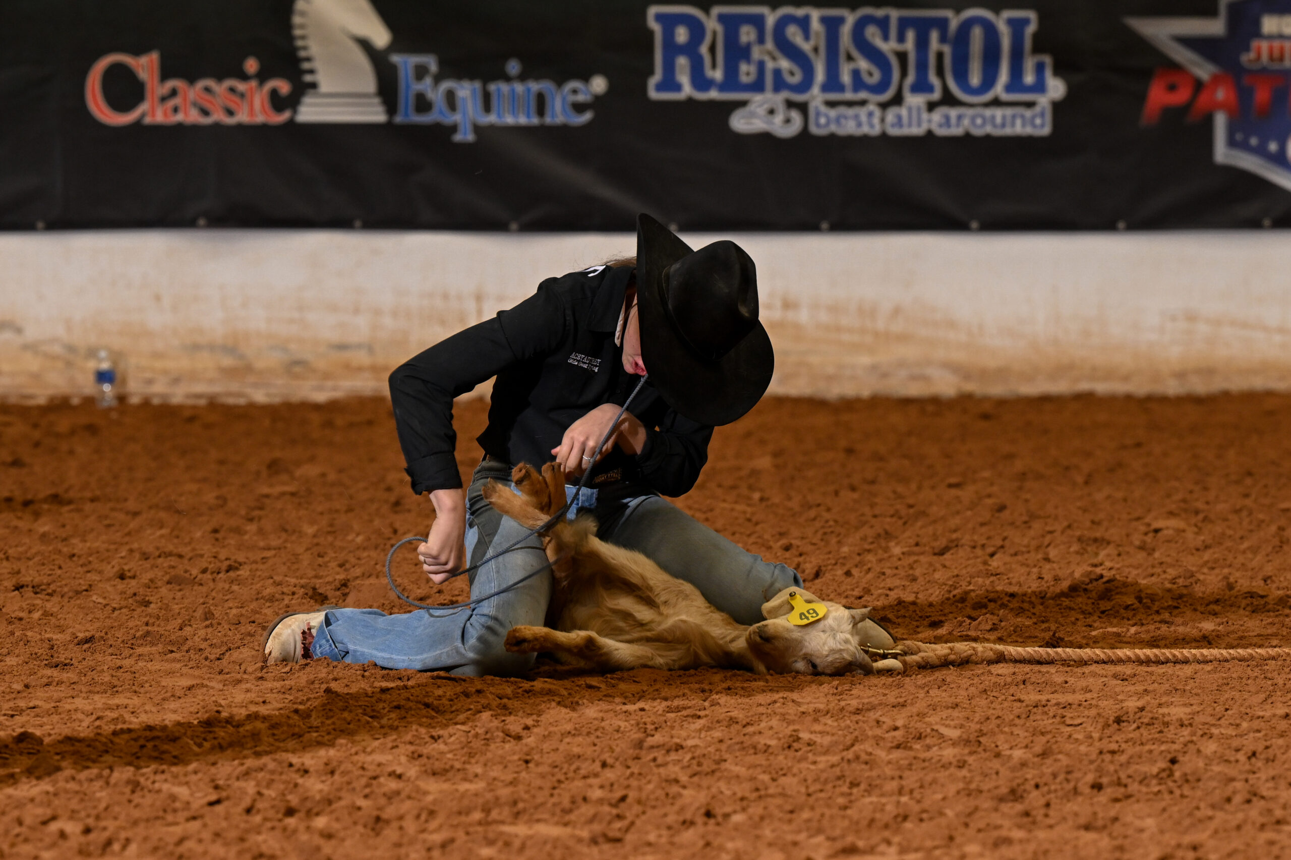 Competitor on ground wrestling a steer during rodeo event at indoor arena with sponsor banners visible