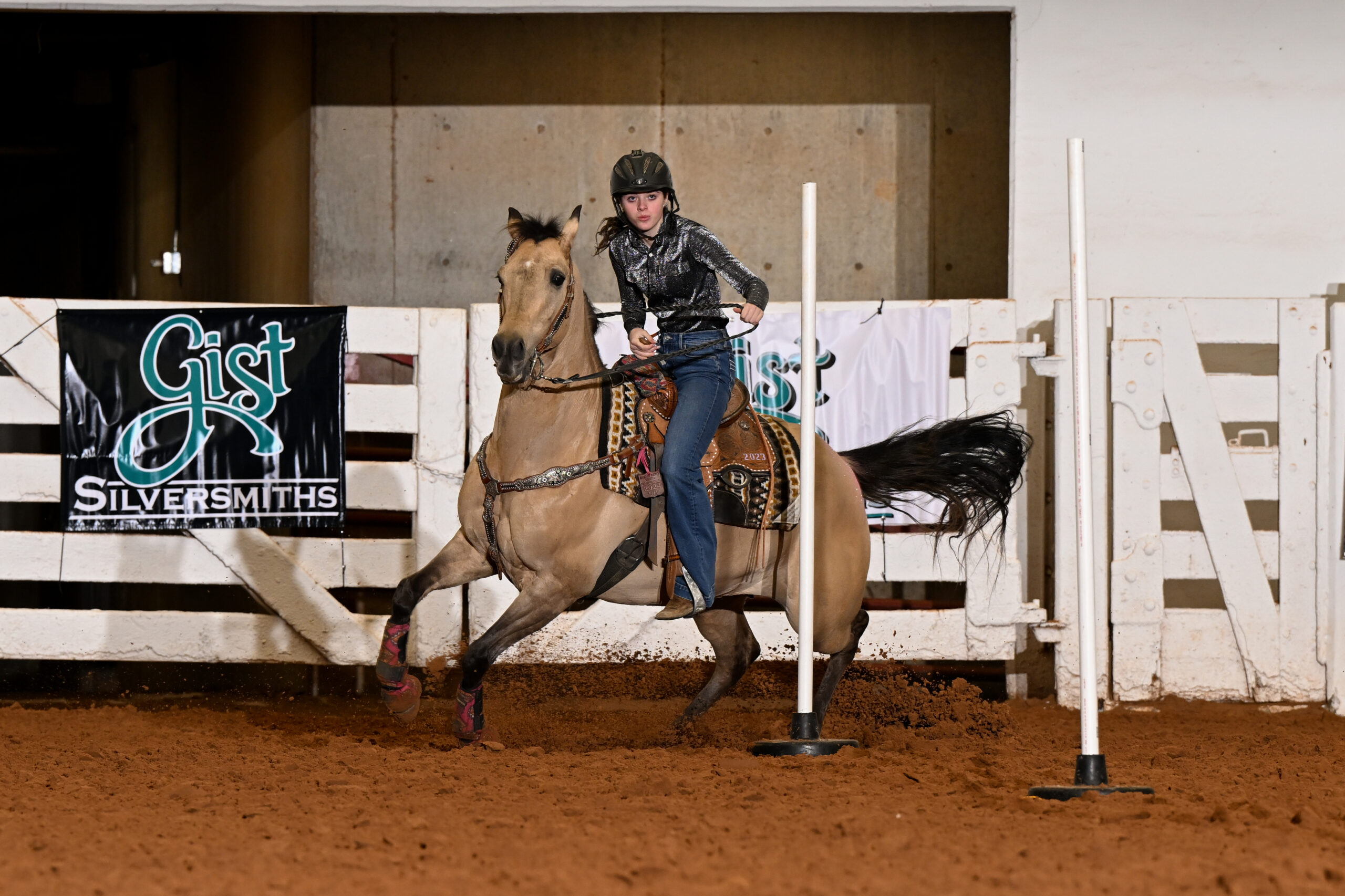 Barrel racer navigates around a white pole on a brown horse during competition at Gist Silversmiths event