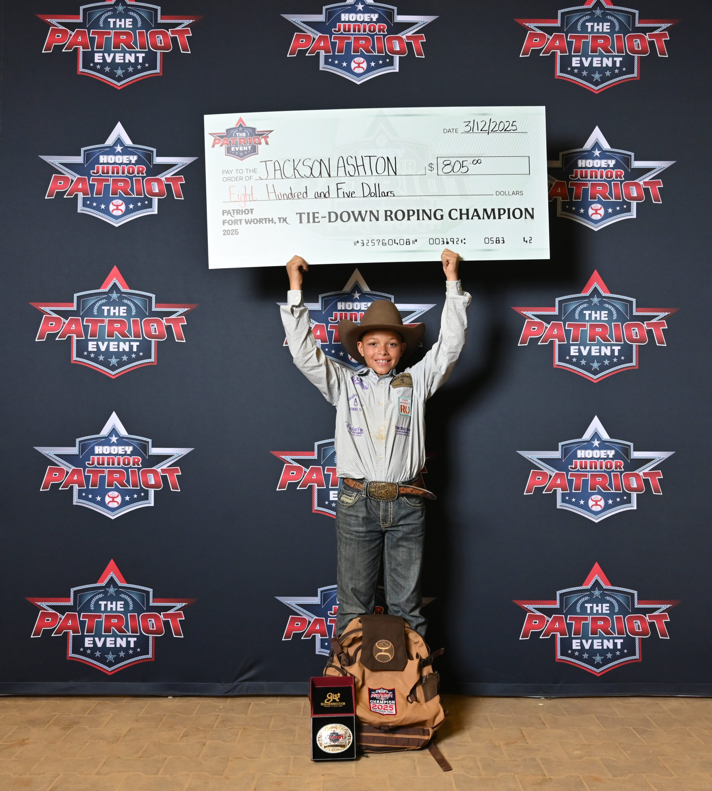 Young boy in cowboy attire holds oversized check for $205 after winning tie-down roping championship at Patriot Event in Fort Worth, Texas on March 12, 2025