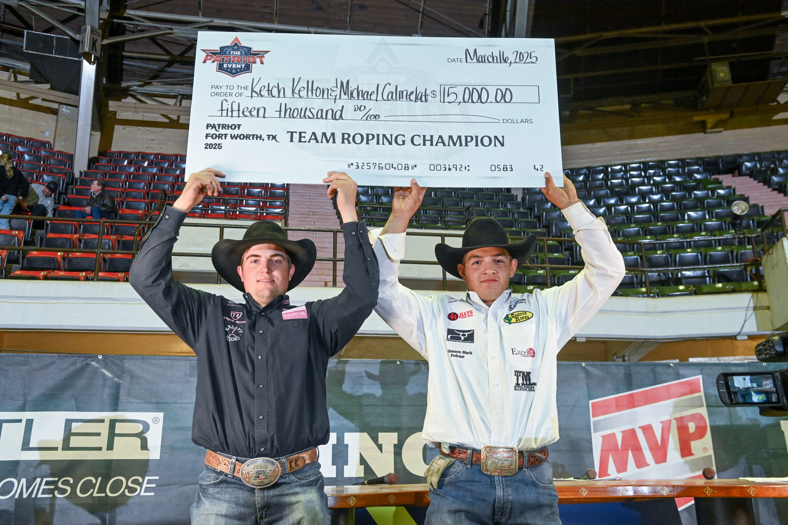 Two team roping champions hold a $115,000 check at the 2025 Patriot Fort Worth event in an arena setting