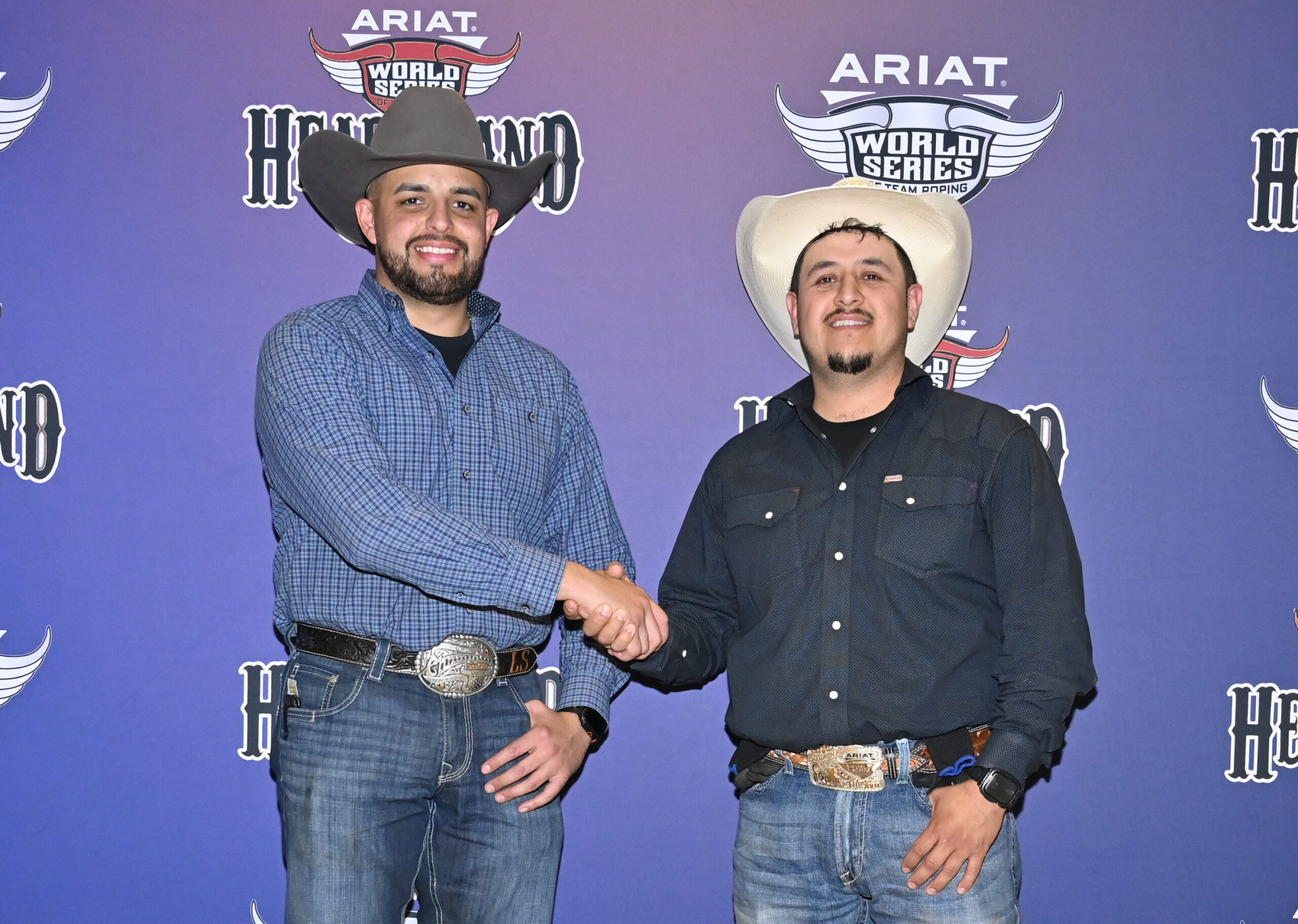 Two team roping competitors shake hands at the Ariat World Series of Team Roping event backdrop